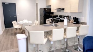 A modern kitchen with a central island, bar stools, and a dining area with chairs. - Lightning Luxe Retreat (Des Moines)