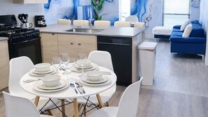 A modern kitchen with a dining area, featuring a marble-like wall mural, a built-in oven, and a dining table set for four. - Lightning Luxe Retreat (Des Moines)
