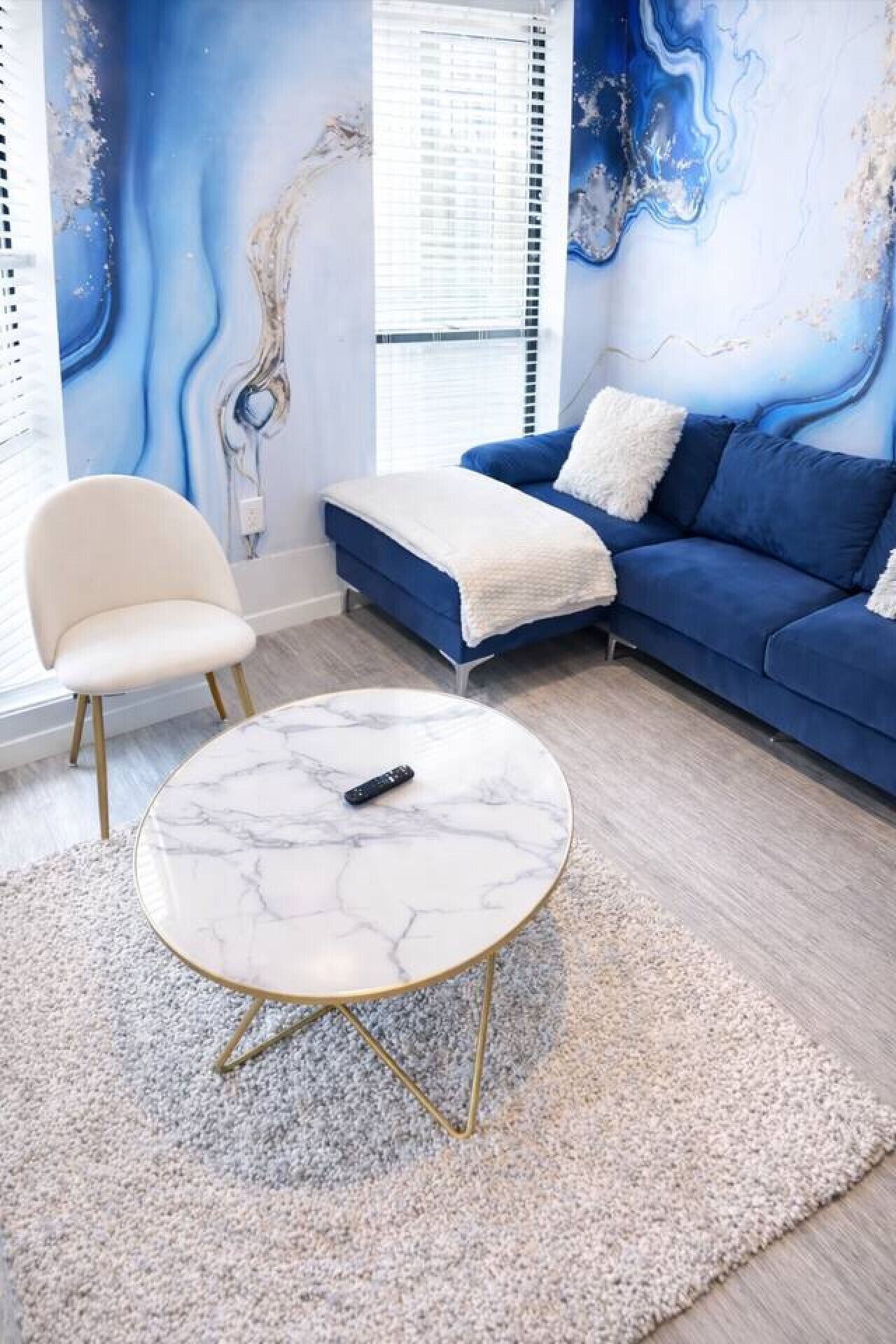 Un salon moderne avec un canapé bleu, un fauteuil blanc et une table basse en marbre.