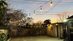 A backyard patio with string lights, a punching bag, and a brick floor.