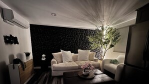 A modern living room with a dark textured wall, a beige sofa, a coffee table with a plant, and a white armchair.