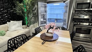 A modern kitchen with an open refrigerator, a dining table with chairs, and a sofa with cushions.