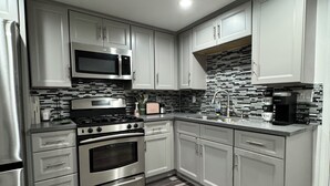 A modern kitchen with stainless steel appliances, white cabinets, and a patterned backsplash.