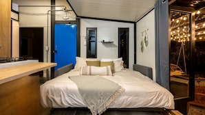 A modern bedroom with a bed, bedside table, and a view of the outdoors.