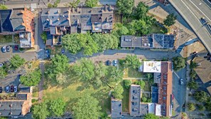 An aerial view of a residential area with multiple buildings, a parking lot, and surrounding greenery. - Massive 5BD/4BA 3-Story Duplex @ Downtown Albany (Albany)