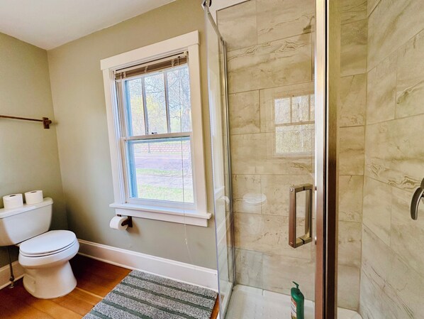 A bathroom with a toilet, a window, a shower with a glass door, and a towel rack.