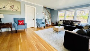 Un salon avec un plancher en bois, deux fauteuils, un canapé, une table basse et un escalier.
