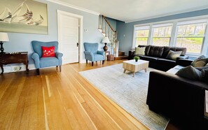 Un salon avec un plancher en bois, deux fauteuils, un canapé, une table basse et un escalier.