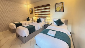 Habitación de hotel con dos camas, un ventanal con persianas, una obra de arte en la pared y una mesita de noche con lámpara.