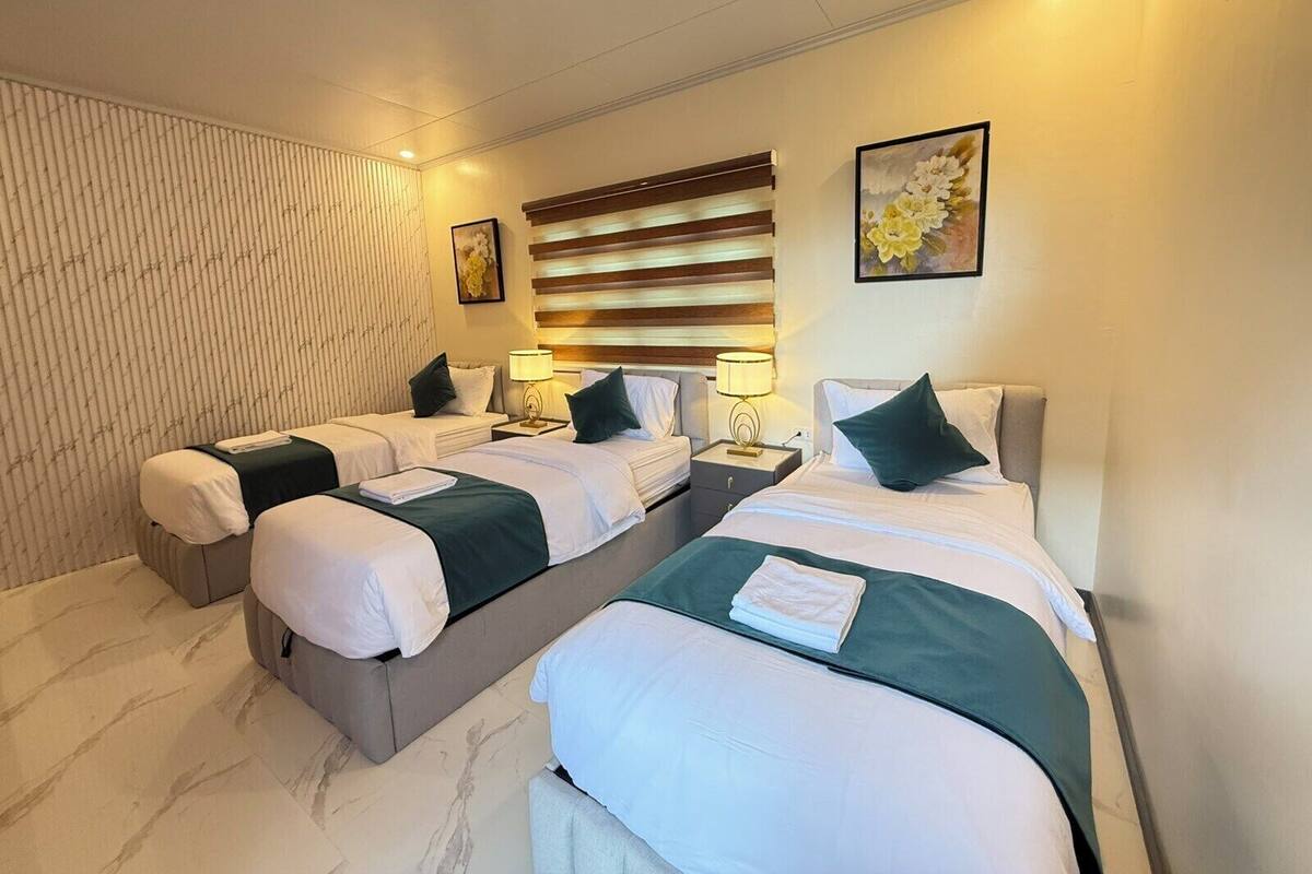 Een hotelkamer met twee bedden, een groot raam met zonwering, een aan de muur hangend kunstwerk en een nachtkastje met een lamp.
