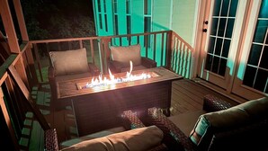 Terraza exterior con una chimenea, mobiliario de mimbre y vistas a una casa.