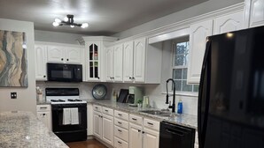 Una cocina moderna con armarios blancos, un refrigerador negro, una encimera de granito y una lámpara en el techo.