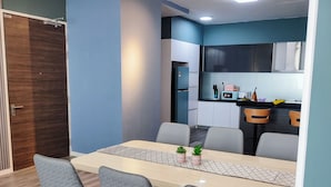 Un espace repas moderne avec une longue table, quatre chaises grises et une cuisine en arrière-plan.