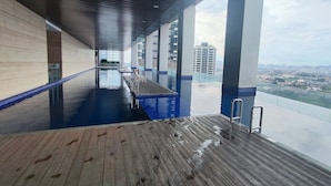 Une piscine intérieure moderne dotée d’une plage en bois, de grandes fenêtres et offrant une vue sur le paysage urbain.