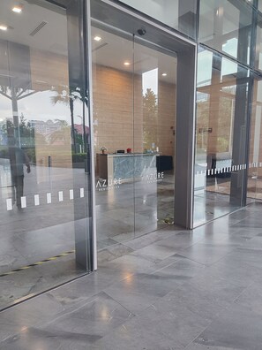Een receptiezone met glazen deuren, een receptiebalie en een bord met daarop Azure Residences.