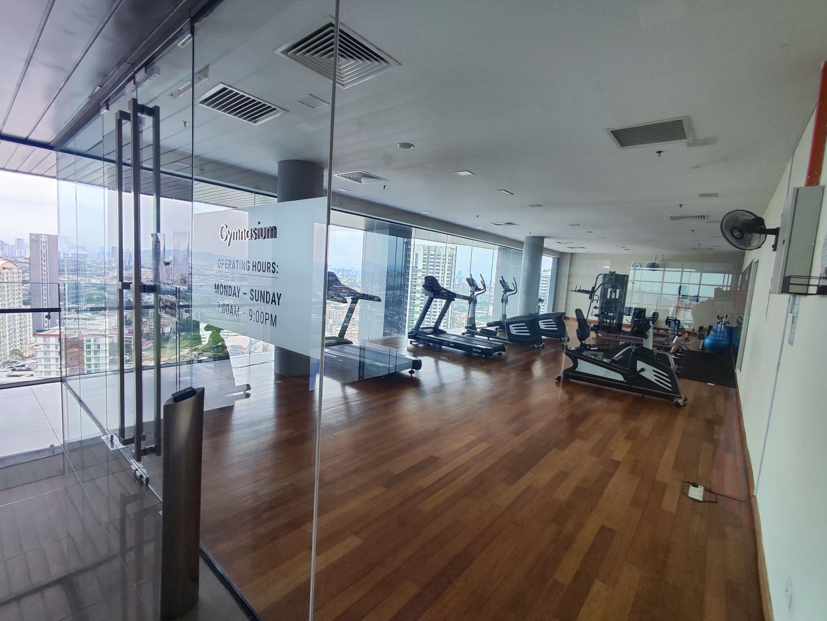 A gym with cardio equipment, weight machines, and a large window offering a city view.