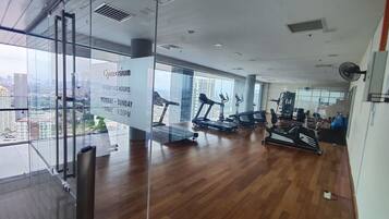 A gym with cardio equipment, weight machines, and a large window offering a city view.
