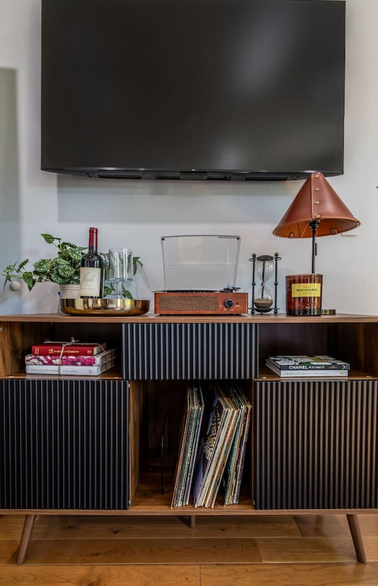 Un salón moderno con un televisor de pantalla plana montado en la pared, una radio antigua, una lámpara y una estantería con libros y objetos decorativos.