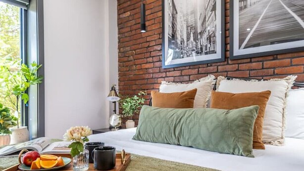 Ein modernes Schlafzimmer mit einer Wand aus Backsteinen, einem großen Bett mit vielen Kissen und gerahmten Bildern darüber.