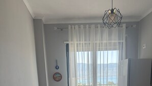 A small living area with a sofa, a table, and a refrigerator. There is a window with sheer curtains and a view of the outdoors. - Modern seaview apartment just 5 min from restaurants and markets, free parking!” (Vlora)