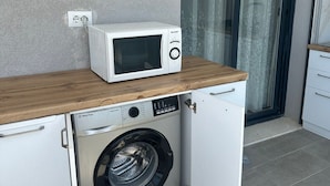 A compact kitchen with a microwave on a wooden countertop, a washing machine, and a sliding glass door to the right. - Modern seaview apartment just 5 min from restaurants and markets, free parking!” (Vlora)