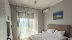 A bedroom with a large bed, a TV, a ceiling light, and a painting on the wall. - Modern seaview apartment just 5 min from restaurants and markets, free parking!” (Vlora)