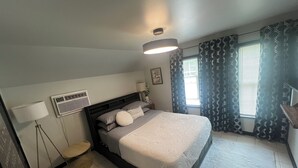 Una camera da letto con un letto, una lampada da comodino, un condizionatore d'aria a parete e tende a motivi.