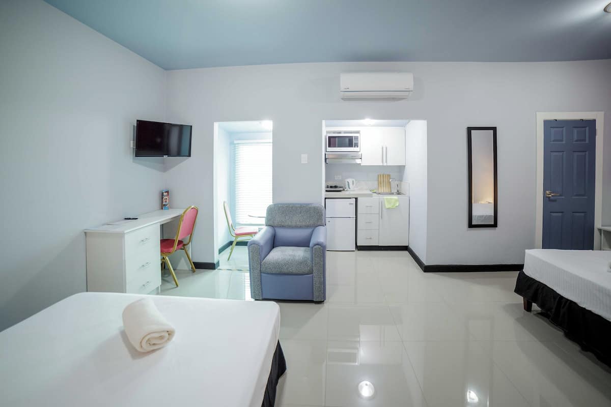 A hotel room with a bed, a desk, a chair, a kitchenette, and a TV.