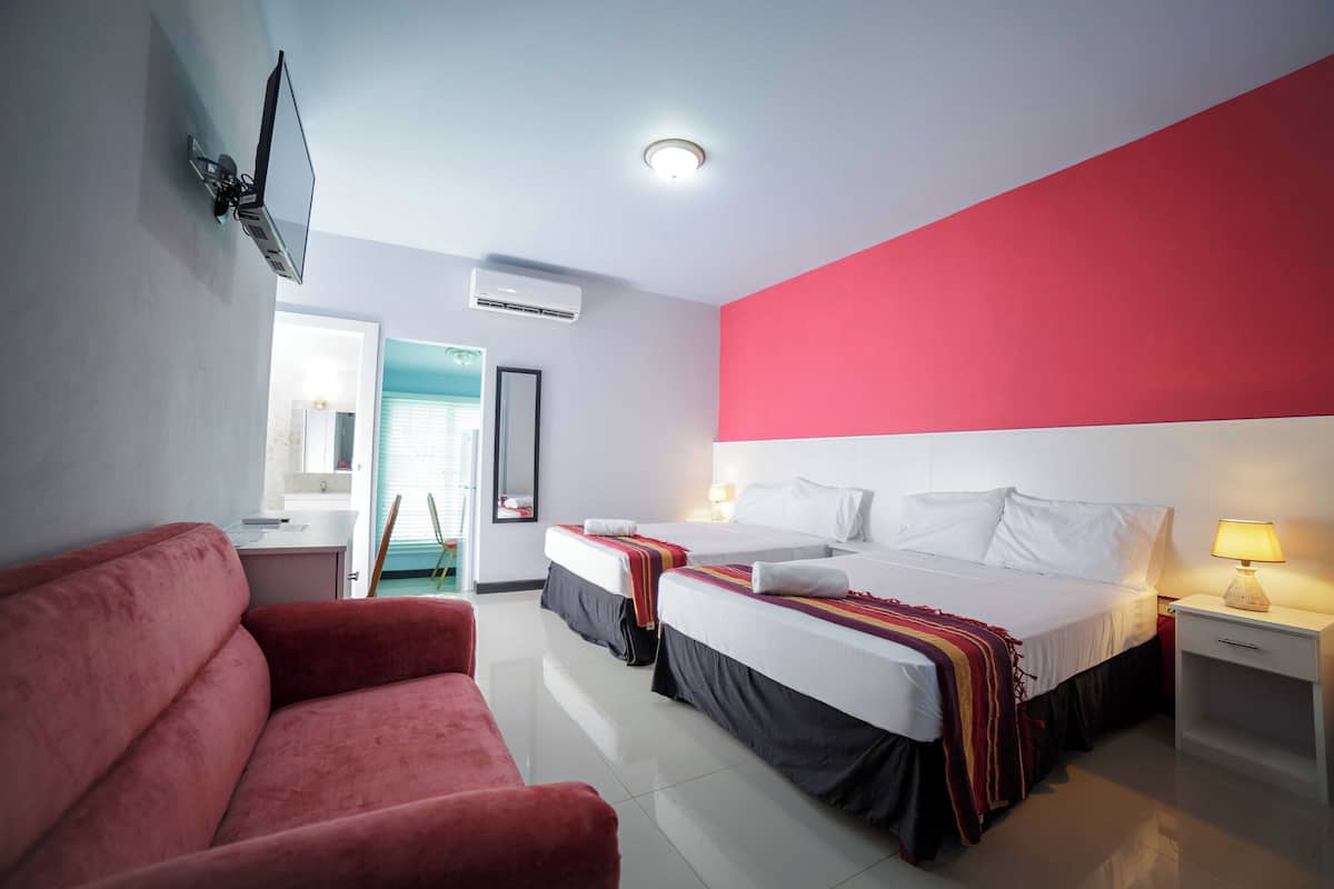 A hotel room with two beds, a red couch, a TV mounted on the wall, and a window with a view of the outside.