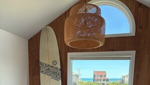 Ein Essbereich mit einem langen Tisch, Stühlen, einem Surfbrett, einem Topf mit Pflanze und Blick auf den Ozean.