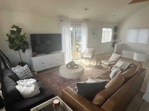 Una sala de estar con televisor, sofás, una mesa de centro y una planta grande.