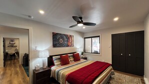 A bedroom with a bed, a ceiling fan, a window, and a door.