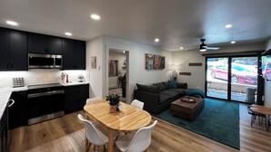 A modern kitchen with dark cabinets, a microwave, and a dining area with a wooden table and white chairs.