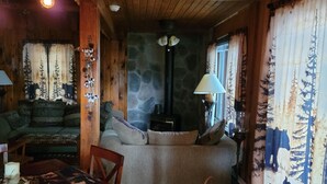 A cozy cabin interior with a stone wall, wooden ceiling, a sofa, a dining table with chairs, and a fireplace. - Charming 2-bedroom  lakefront cabin in delightful Phillip,WI (Phillips)