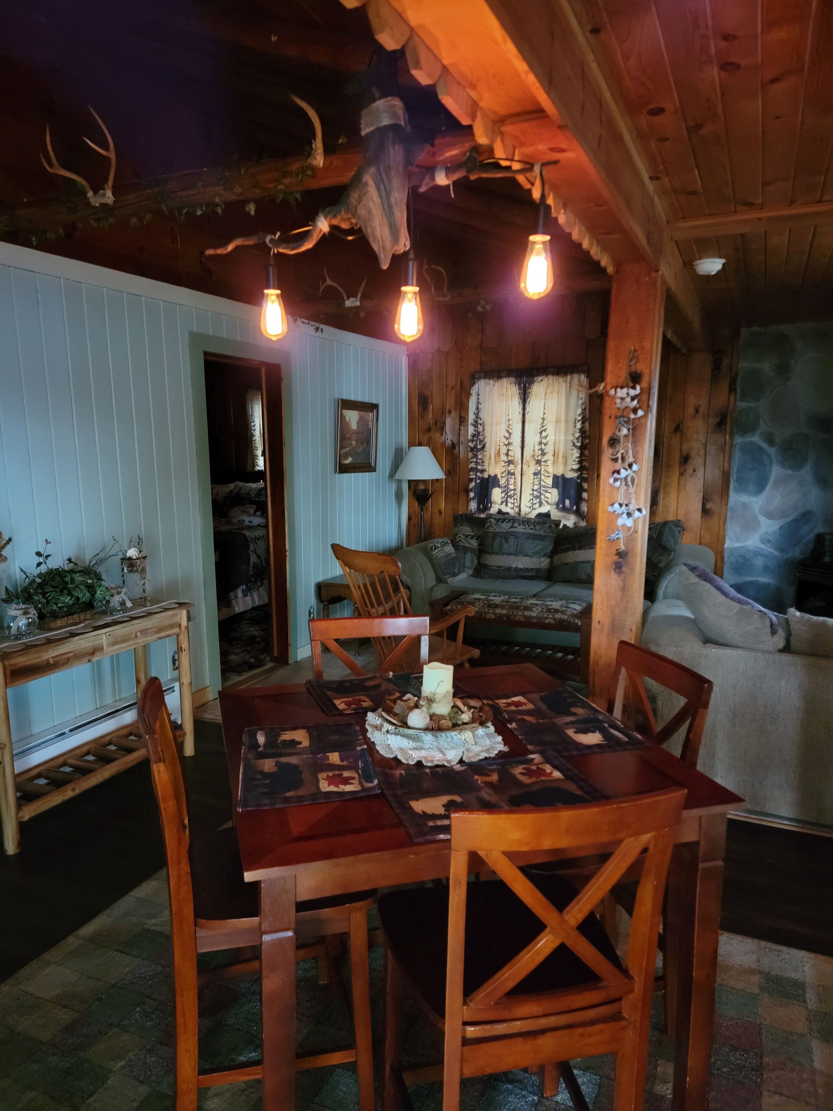 Interior acollidor d'una cabana amb taula de dinar de fusta, cadires i una llar de foc.