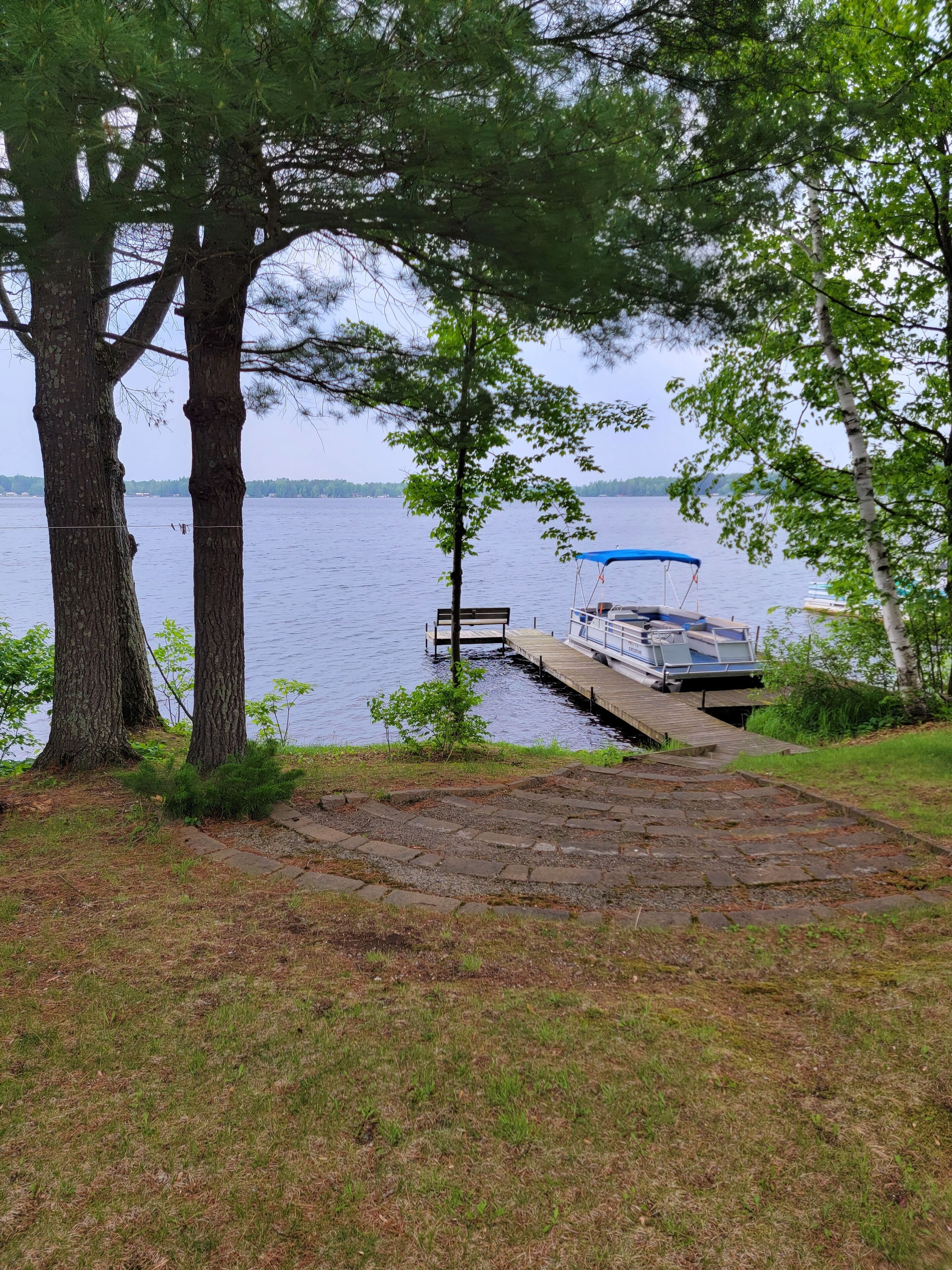 A dock extending into a calm lake, surrounded by trees and grassy areas.