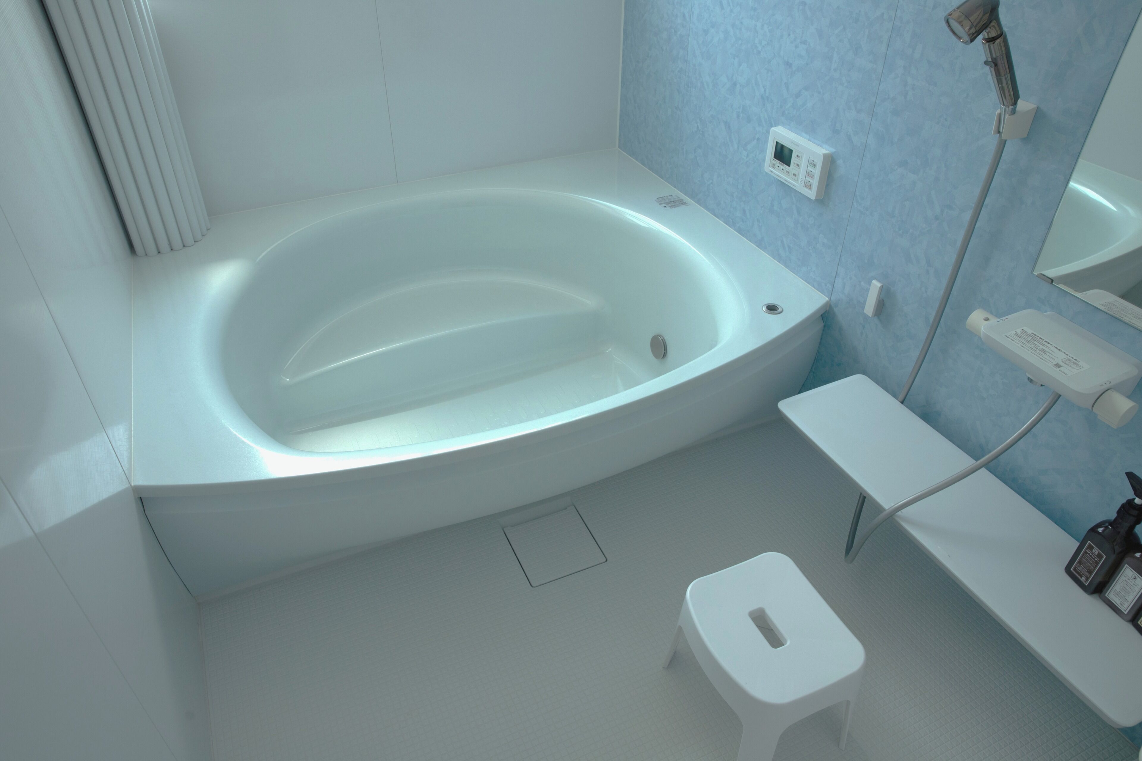 Un baño moderno con una bañera independiente, un taburete pequeño, un tocador con espejo y un cabezal de ducha de mano.