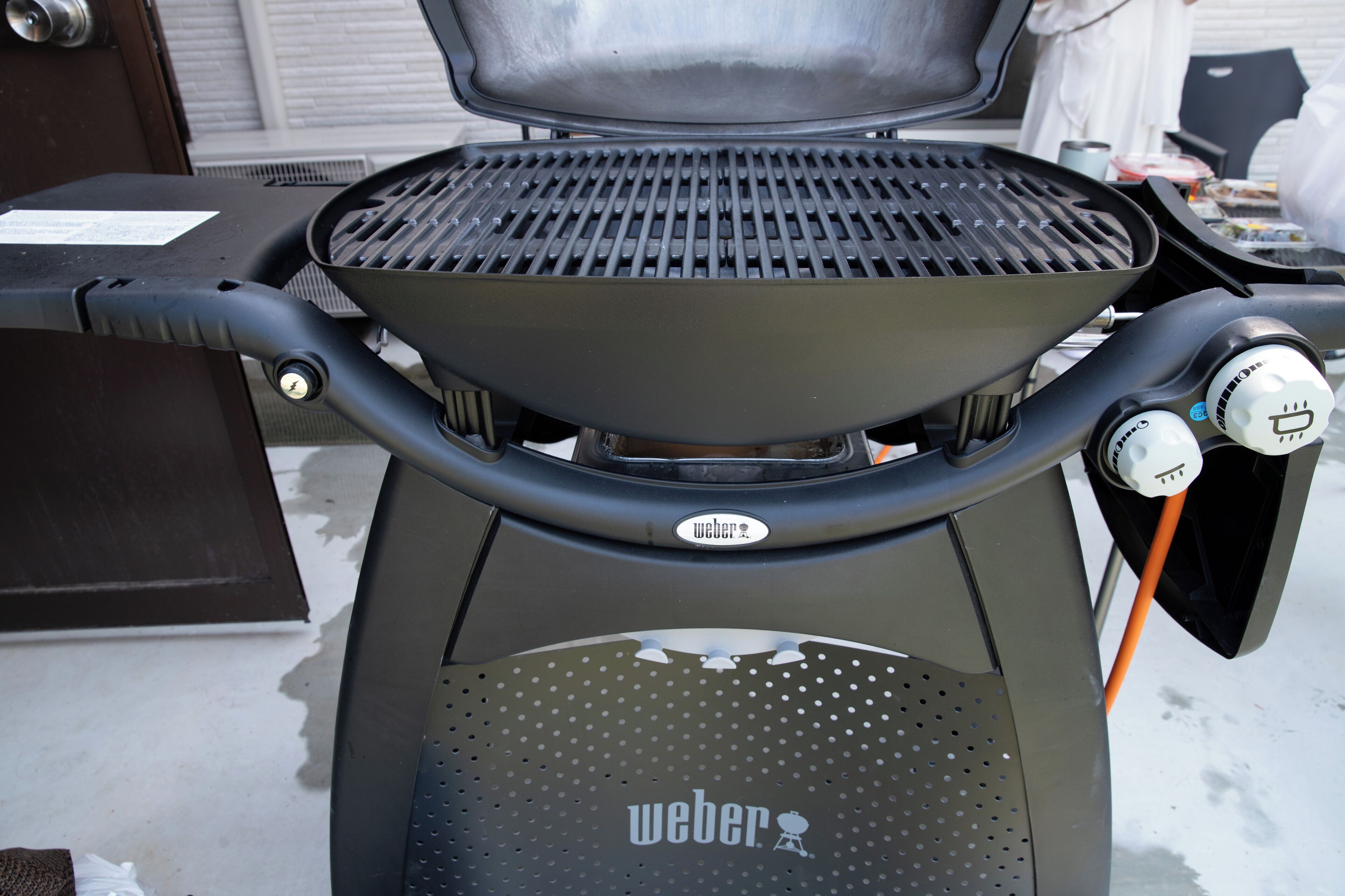A Weber grill with a control panel and a perforated footrest.