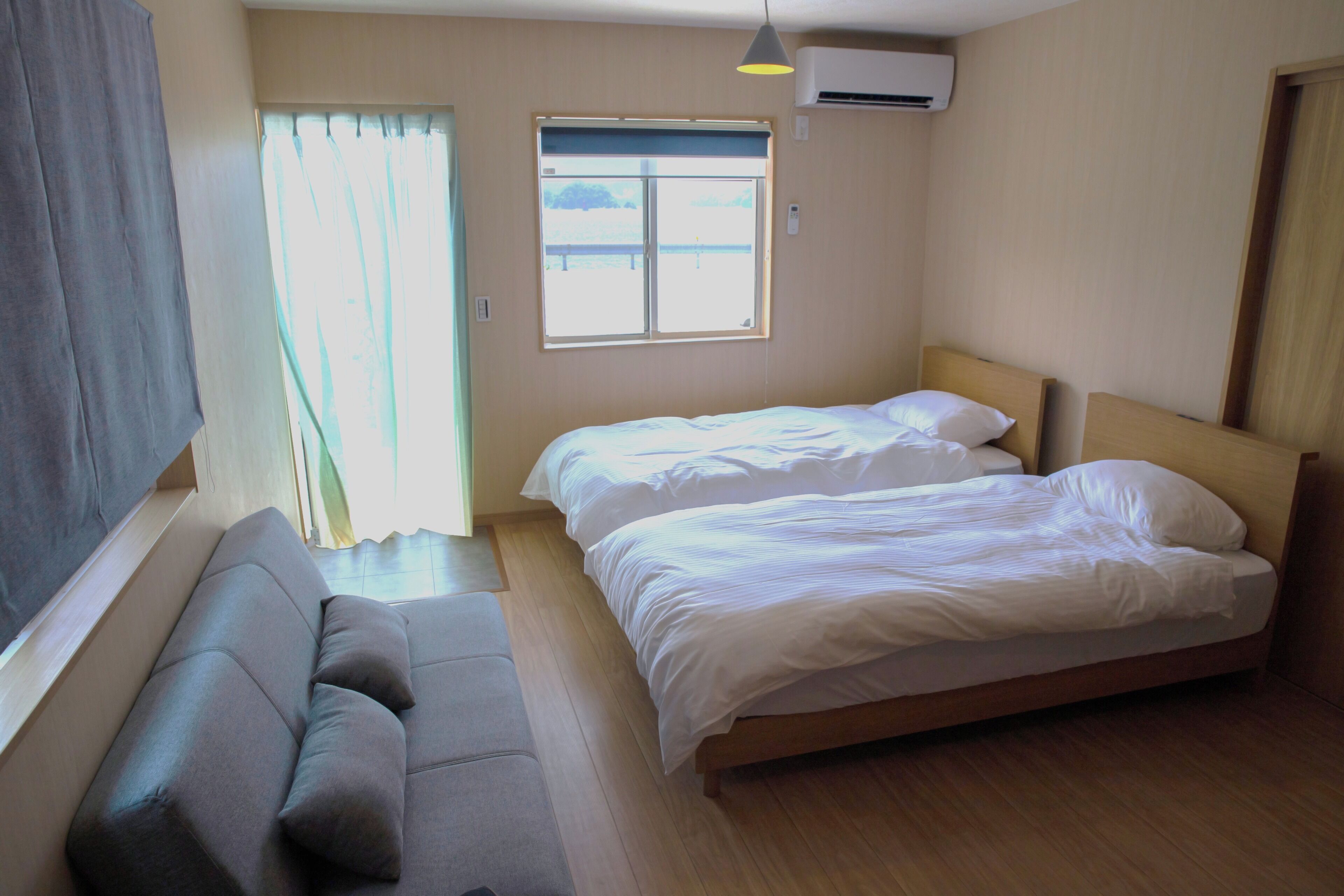 A room with two beds, a sofa, a window with curtains, and an air conditioning unit.