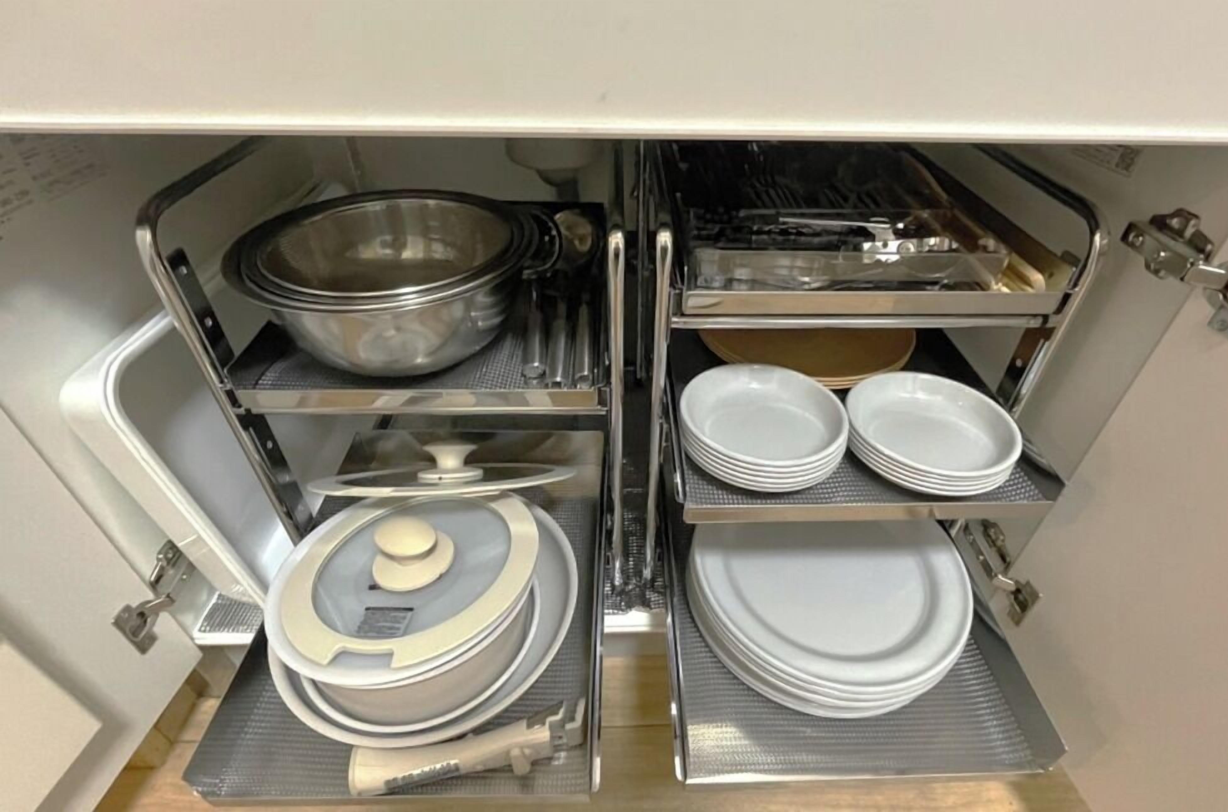 Una cocina con electrodomésticos de acero inoxidable, incluyendo estufa, horno y lavaplatos. Hay varios utensilios de cocina y vajilla guardados en estanterías.