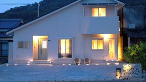 A two-story building with a light-colored exterior, a front entrance with a door, two windows with curtains, and a small balcony. - SANTE 4073 STAY & SAUNA HAKATA ISLAND 1 (Imabari)