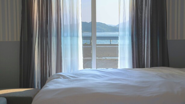 A hotel room with a large bed, a view of a body of water, and sheer curtains. - SANTE 4073 STAY & SAUNA HAKATA ISLAND 1 (Imabari)