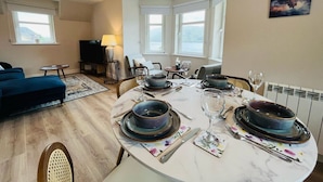 Een eetgedeelte met een ronde tafel voor vier personen, omringd door stoelen. Achtergrond is een bank en een televisie.