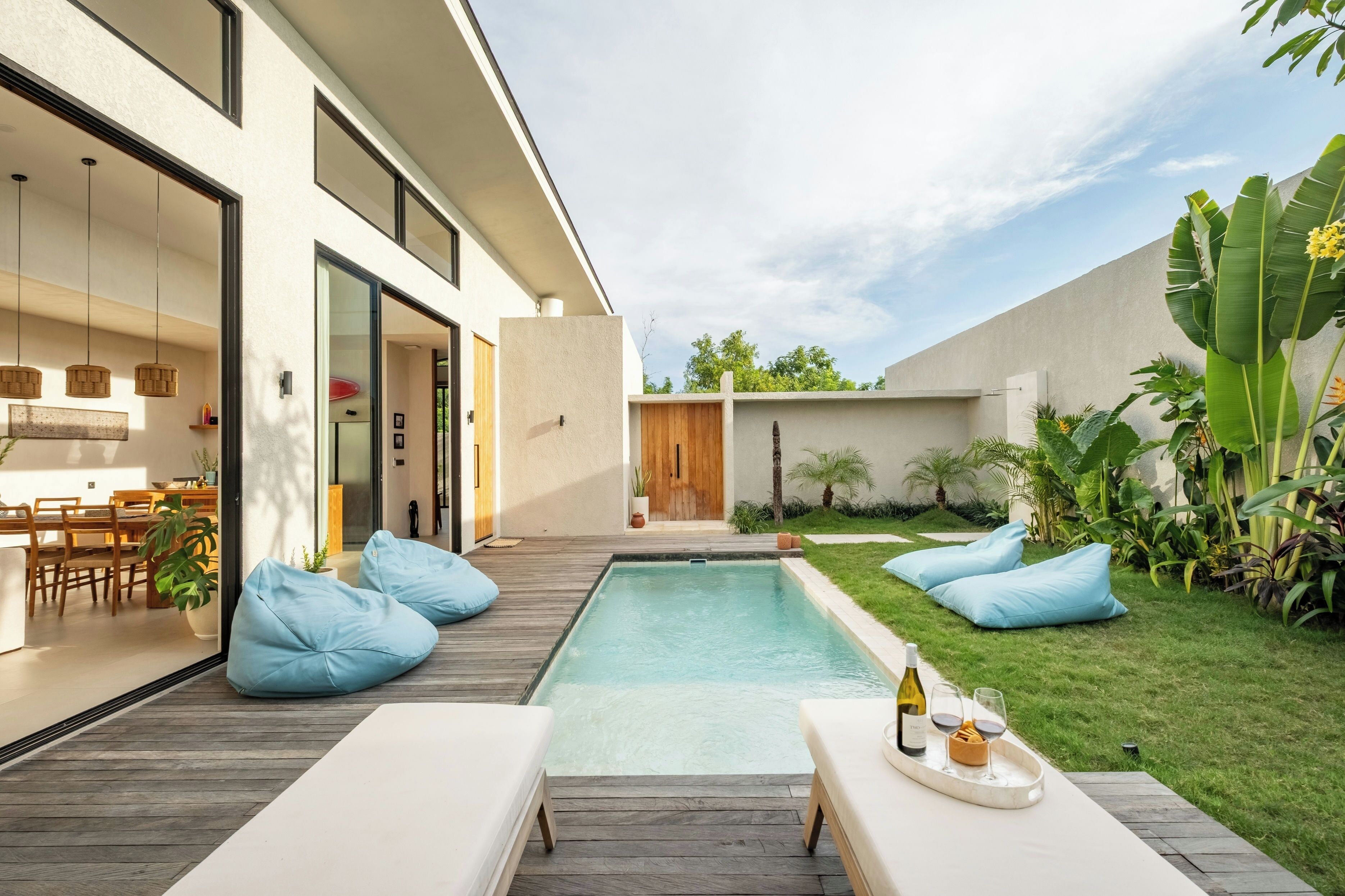 A modern outdoor pool area with a wooden deck, lounge chairs, and a dining area with a table and chairs.
