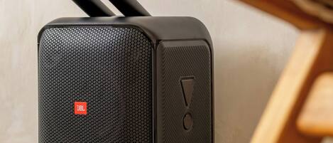 A black portable speaker with JBL branding, placed on a tiled floor next to a wooden chair.