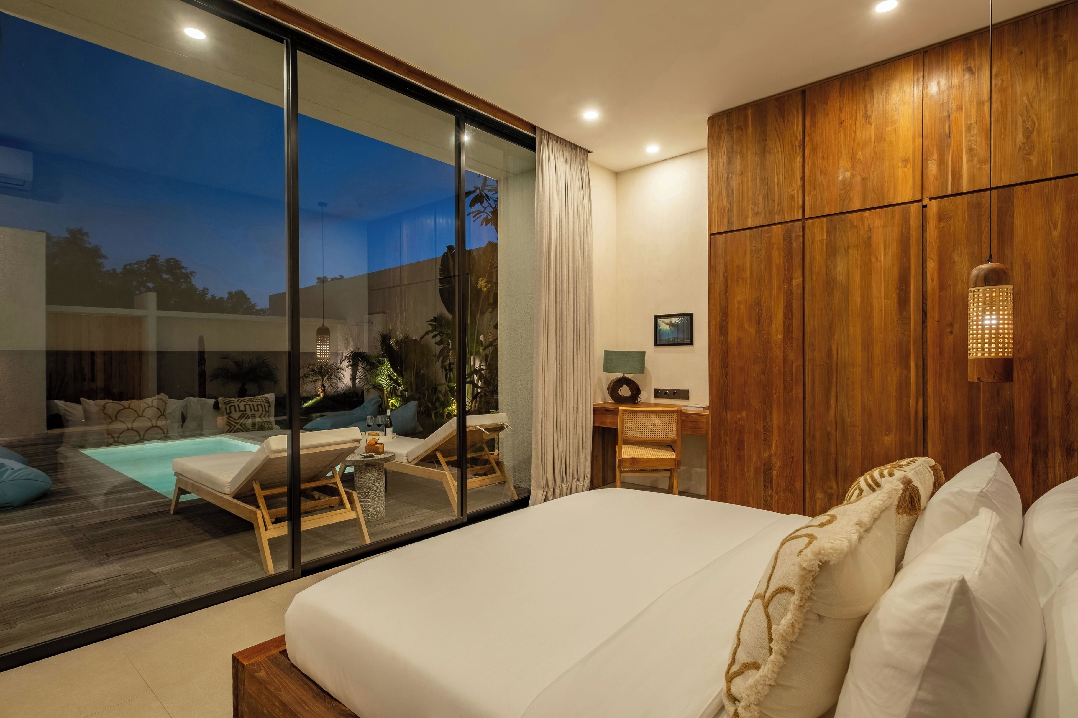 Une chambre moderne avec un grand lit, une armoire en bois, un bureau et une vue sur une piscine extérieure.