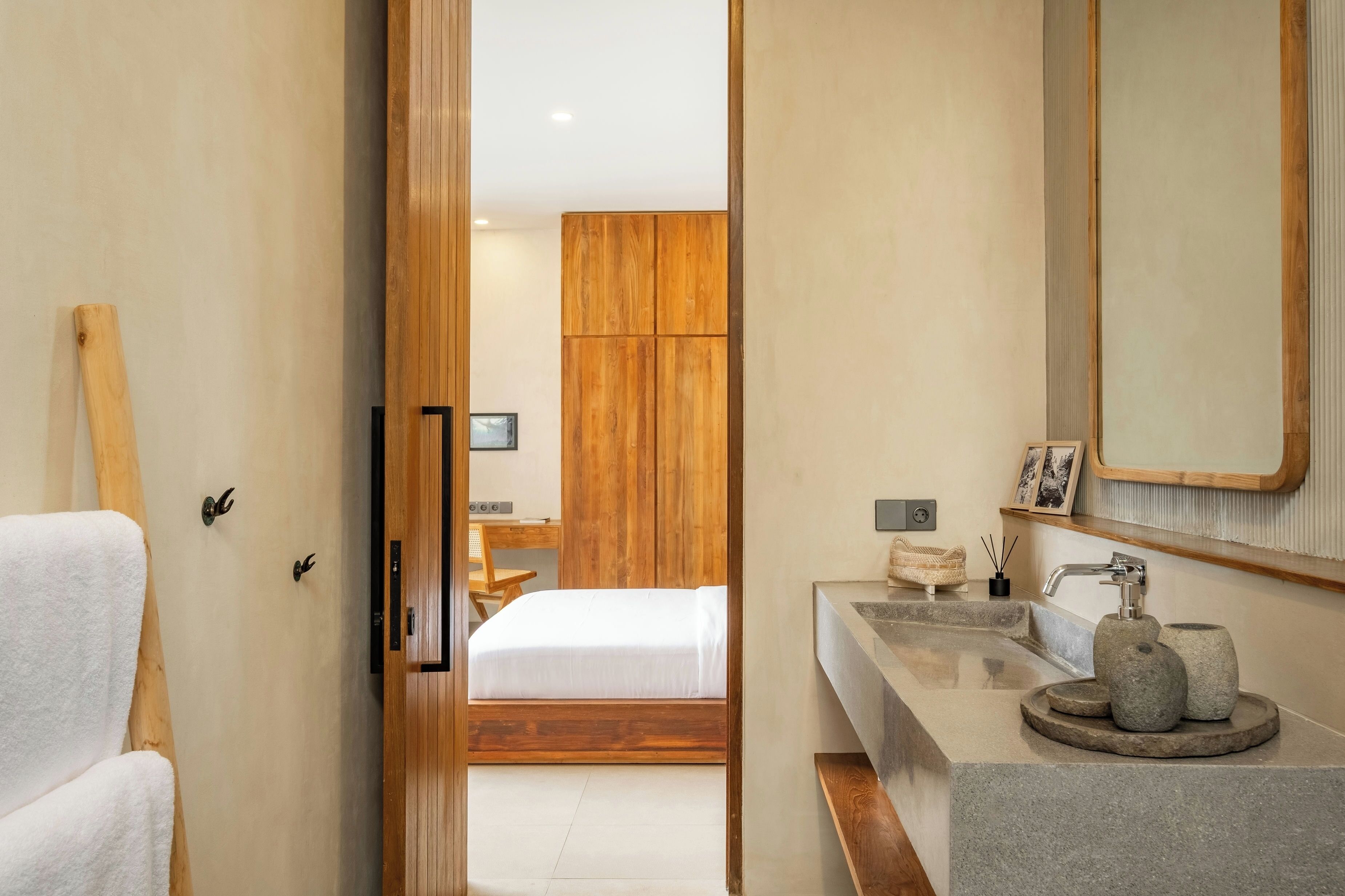 A modern bathroom with a wooden vanity, a large mirror, and a bed in the background.