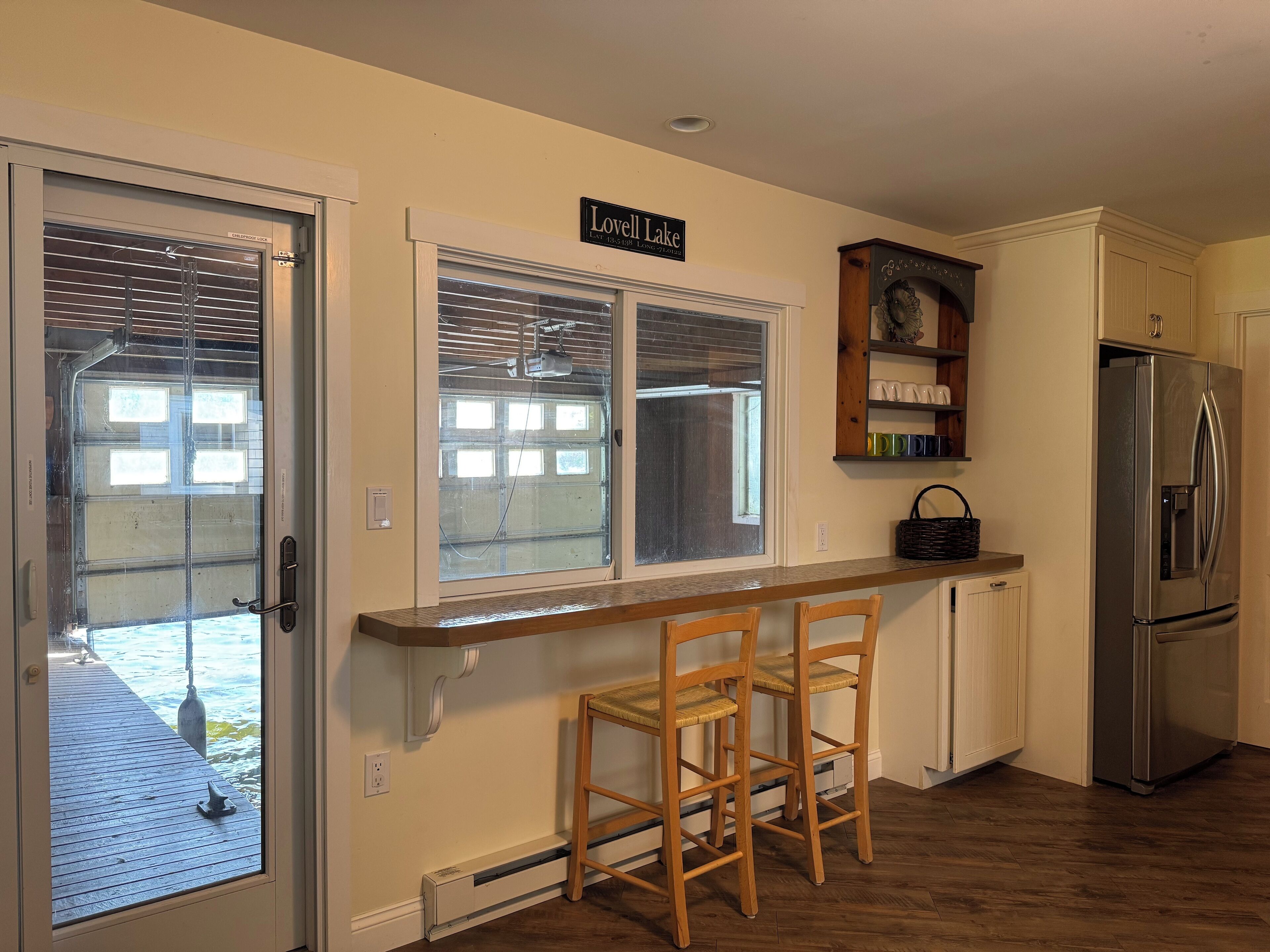 Une cuisine avec un comptoir-bar en bois, deux tabourets de bar en bois, un réfrigérateur en acier inoxydable et une enseigne indiquant «Lovell Lake».