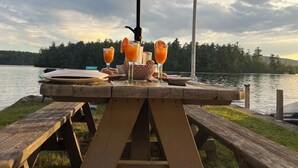 A picnic table with drinks and bread, overlooking a lake with a boat in the background.