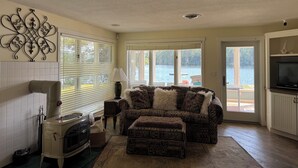 A cozy living room with a fireplace, a sofa, and a view of a lake through large windows.